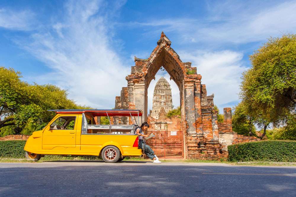 Une touriste prend une photo à côté d'un minibus à côté d'un temple à Ayutthaya